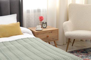 Yatağın yanında kahve, çiçek ve çalar saat olan komodinin yanında.