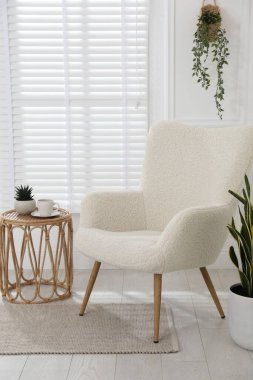 Rahat koltuk, yan masa ve beyaz duvarın yanındaki bitkiler.
