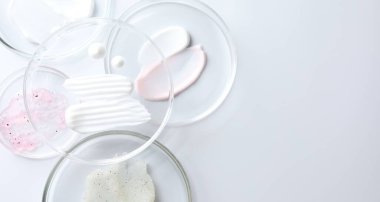 Petri kabında farklı kozmetik ürünleri, beyaz arka planda, düz yerde. Metin için boşluk