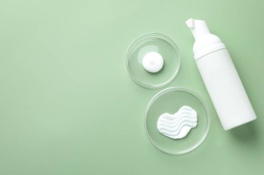 Petri kaplarında farklı kozmetik ürünler ve yeşil arka planda bir şişe, düz yatak. Metin için boşluk