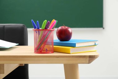 Farklı okul kırtasiyesi ve tahtanın yanındaki ahşap masada kırmızı elma.