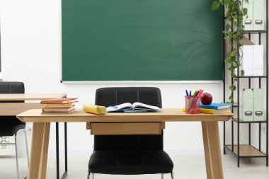 Farklı okul kırtasiyesi ve kırmızı elma, kapalı alanda tahtaya yakın ahşap masada.