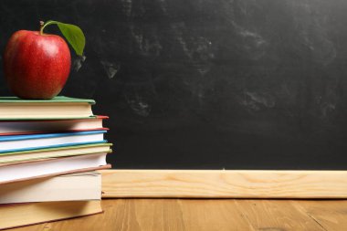 Tahtanın yanındaki ahşap masada farklı kitaplar ve kırmızı elma, yakın plan. Metin için boşluk