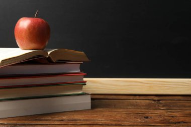 Tahtanın yanındaki ahşap masada farklı kitaplar ve elmalar, yakın plan. Metin için boşluk