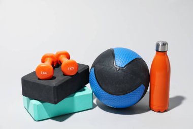 İlaç topu, dambıl, su şişesi ve açık gri arka planda köpük blokları.
