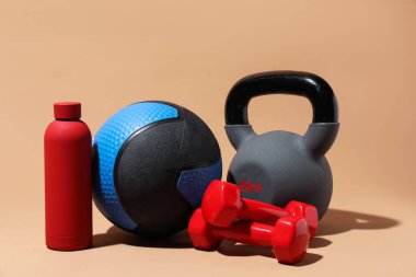 İlaç topu, halterler, su şişesi ve bej arka planda su ısıtıcısı.
