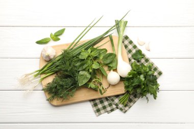 Farklı taze otlar, yeşil soğanlar ve sarımsak beyaz ahşap masa, düz uzanmış.