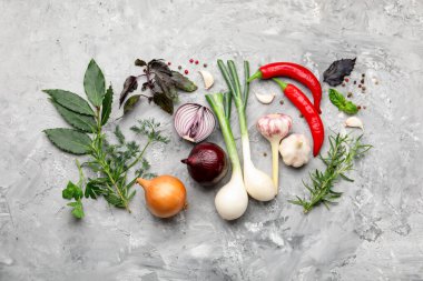 Farklı taze otlar, sarımsak, soğan ve diğer baharatlar gri masada, düz yerde.