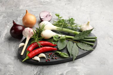 Farklı taze otlar, sarımsak, soğan ve diğer baharatlar gri masada, yakın plan.