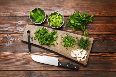 Farklı taze otlar, baharatlar ve bıçaklar ahşap masada, düz yerde.