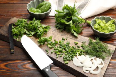 Farklı taze otlar, baharatlar ve bıçaklar ahşap masada, yakın plan.