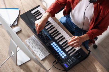 İçerideki ahşap masada MIDI klavyesiyle çalışan bir adam.