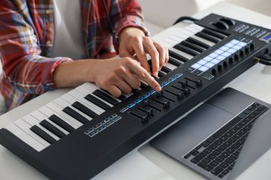 Beyaz masada MIDI klavyesiyle çalışan adam, yakın plan.