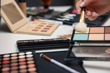 Makyaj masasında fırça ve kapatıcı paleti olan kadın, yakın plan.