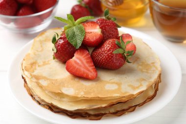 Çilekli leziz krepler, bal, nane ve çay beyaz masada, yakın plan.