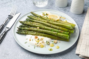 Lezzetli pişmiş kuşkonmaz, limon ve sosla servis edilir. Gri masada, yakın plan.