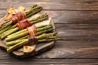 Ahşap masada domuz pastırması ve patatesle servis edilen lezzetli pişmiş kuşkonmaz. Metin için boşluk