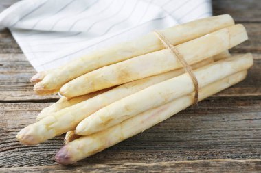 Ahşap masada çiğ beyaz kuşkonmaz mızrakları, yakın plan.