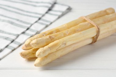 Beyaz ahşap masada çiğ kuşkonmaz mızrakları, yakın plan.