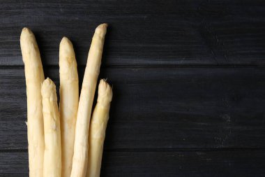 Çiğ beyaz kuşkonmaz mızrakları siyah ahşap masada, düz yerde. Metin için boşluk