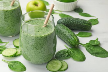 Lezzetli ıspanaklı smoothie ve malzemeler beyaz masada, yakın plan.