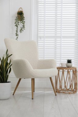 Rahat koltuk, yan masa ve beyaz duvarın yanındaki bitkiler.
