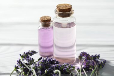 Beyaz ahşap masada doğal yağ ve lavanta çiçekleri, yakın plan.