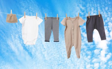 Mavi gökyüzüne karşı çamaşır ipinde kurumuş farklı bebek kıyafetleri.
