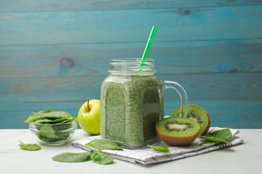 Mason kavanozundaki lezzetli smoothie, ıspanak yaprakları, kivi ve elma beyaz masada açık mavi ahşap arka planda, yakın plan