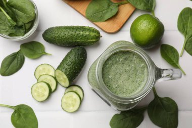 Mason kavanozundaki lezzetli smoothie, ıspanak yaprakları, kireç ve salatalık beyaz fayanslı masada, düz yerde.