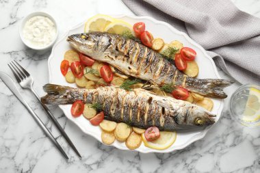 Beyaz mermer masada patates, domates, sos ve limonla servis edilen kızarmış deniz kabuğu balığı. Ev yapımı deniz ürünleri yemeği.