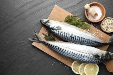 Deniz ürünleri lezzetleri. Taze çiğ uskumrular ve baharatlar siyah masada, düz yerde. Metin için boşluk