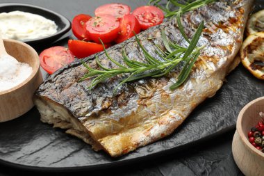 Lezzetli kızarmış uskumru, siyah masada baharat ve sosla servis ediliyor, yakından. Ev yapımı deniz ürünleri yemeği.