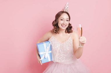 Doğum günü kutlaması. Bir bardak köpüklü şarap ve pembe arka planda bir hediye.