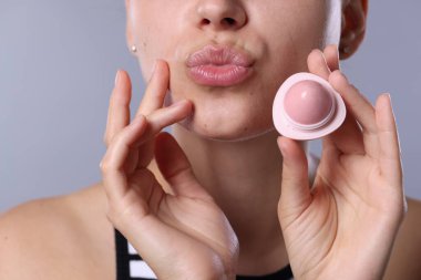 Açık gri arka planda dudak merhemi olan genç bir kadın, yakın plan.