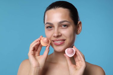 Açık mavi arka planda dudak kremleri olan genç bir kadın.