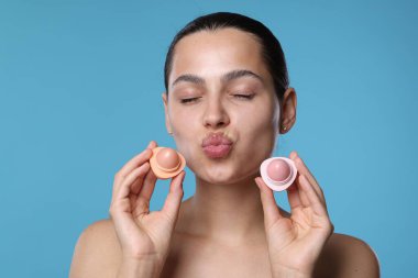 Açık mavi arka planda dudak kremleri olan genç bir kadın.