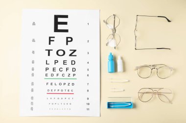 Görme testi çizelgesi, gözlük, cımbız ve bej arka planda tıbbi damlalar, düz yatış