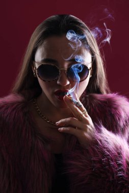 Kürk ceketli güzel bir kadın koyu pembe arka planda sigara içiyor, yakın plan.