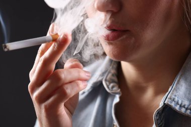 Arka planda sigara içen tişörtlü bir kadın, yakın plan. Kötü alışkanlık.