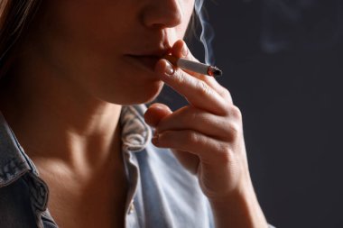 Arka planda sigara içen tişörtlü bir kadın, yakın plan. Kötü alışkanlık.