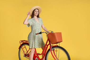 Sarı arka planda sepeti olan şapkalı gülümseyen bir kadın.