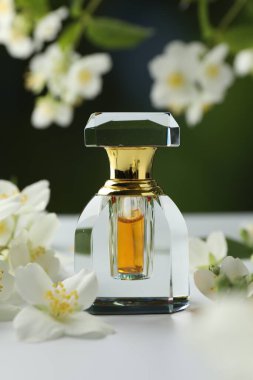 Beyaz masadaki bir şişe parfüm ve yasemin çiçekleri bulanık arka planda, yakın plan