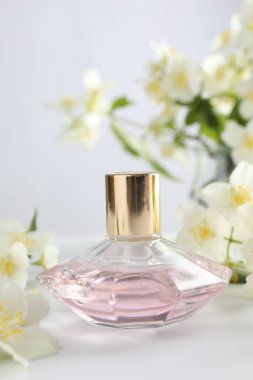 Beyaz masada bir şişe parfüm ve yasemin çiçeği, yakın plan.