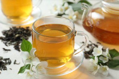 Cam bardakta yasemin çayı, çaydanlık, çiçekler ve kuru yapraklar beyaz masada, yakın plan.