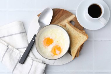 Kâsede yarı haşlanmış yumurta, kahve ve beyaz döşeme üzerinde kızarmış ekmek, düz yatak. Geleneksel Asya kahvaltısı