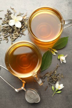 Cam fincanlarda yasemin çayı, gri masada bira ve çiçekler, düz uzanmış