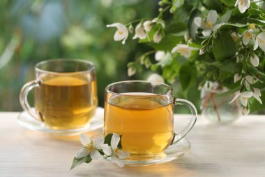 Lezzetli yasemin çayı fincanda ve çiçekler beyaz ahşap masada, yakın plan.