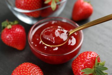 Lezzetli ev yapımı çilek reçeli ve siyah masada kaşık, yakın plan.