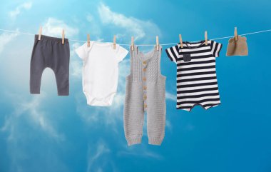 Mavi gökyüzüne karşı çamaşır ipinde kurumuş farklı bebek kıyafetleri.